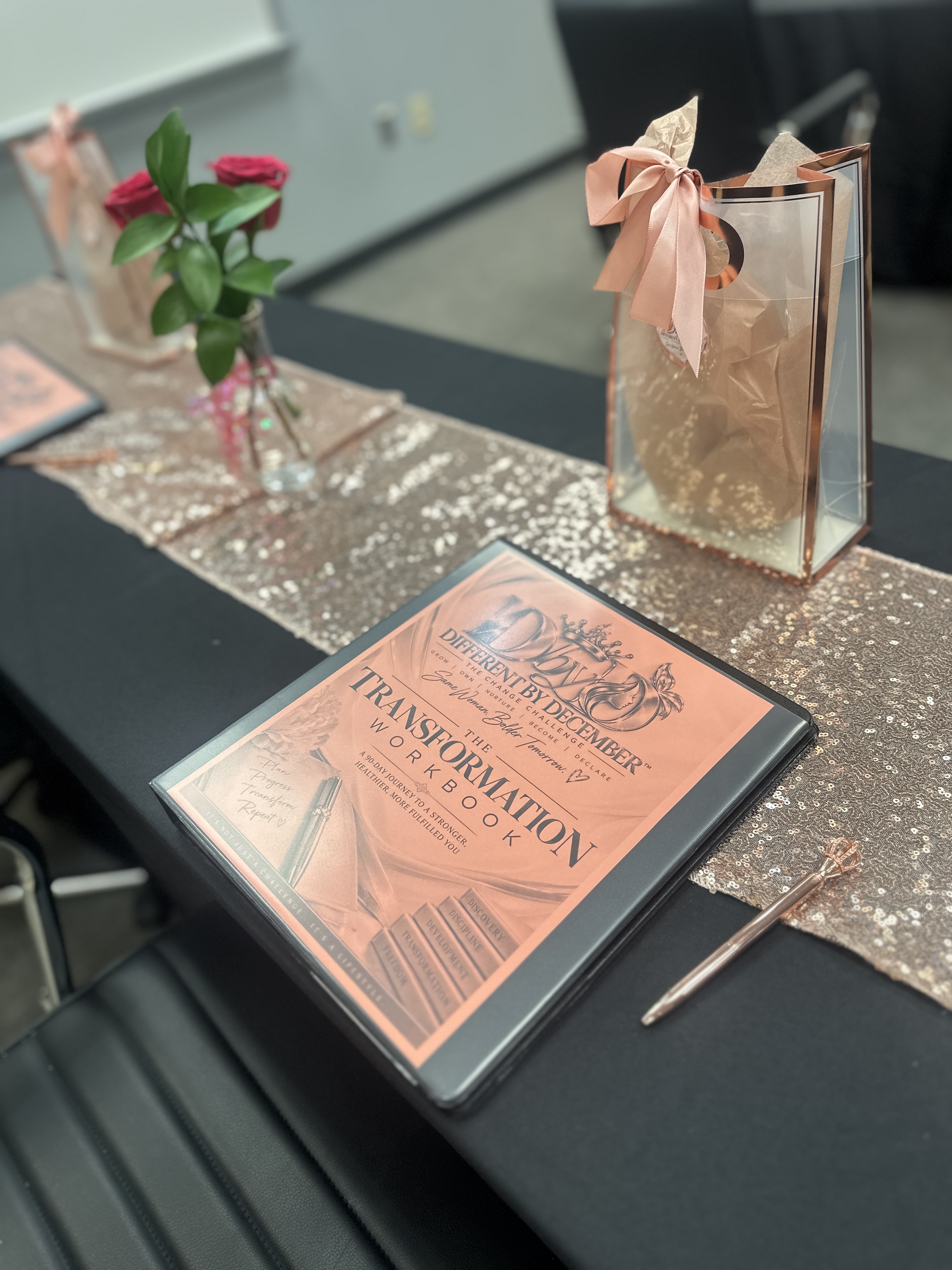 The Different By December Transformation Workbook styled on a rose-gold event table